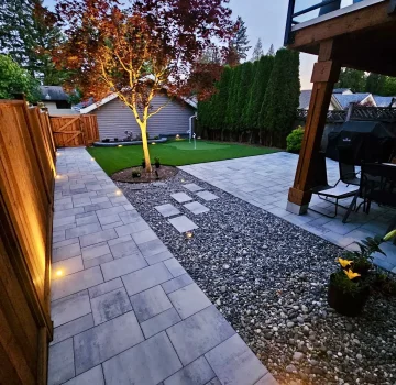 outdoor lighting in a backyard lighting a paver stone path with a rock garden, tree and artificial turf