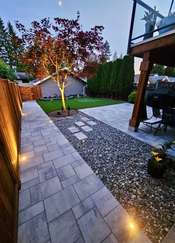 outdoor lighting in a backyard lighting a paver stone path with a rock garden, tree and artificial turf