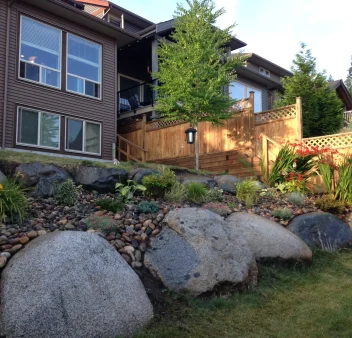 a rock retaining wall the shows two levels of a back yard landscape with small plants in it.